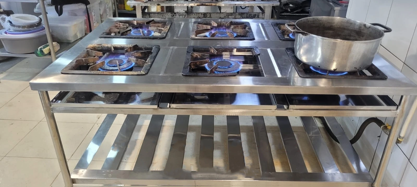 Fogão de seis queimadores em funcionamento com estrutura e prateleira inferior de aço inox